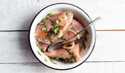 Sea bass marinating in chermoula mix  of  garlic, cumin, coriander,  lemon, onion, ground chili peppers, black pepper, saffron, mint, paprika, salt, oil in pot  on white  wooden background