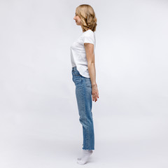 A blonde girl is stands and smiling in a white t-shirt and blue jeans on a white background.