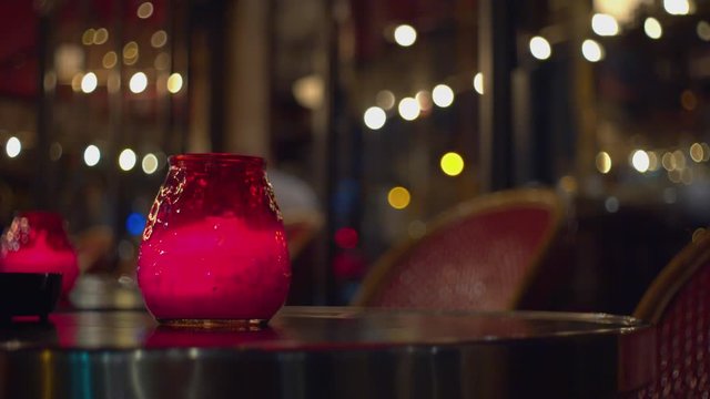 Candle in a red glass on a table in a cafe in the evening