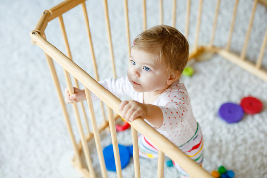 Beautiful Little Baby Girl Standing Inside Playpen. Cute Adorable Child Playing With Colorful Toys. Home Or Nursery, Safety For Kids. Alone Baby Waiting For Mom