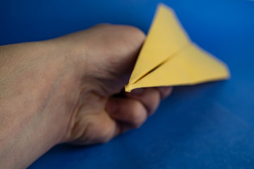 Hand holds paper yellow airplane. Blurred background