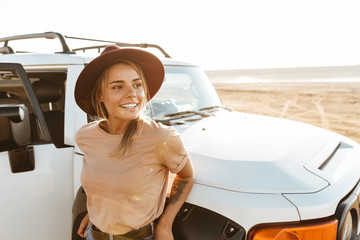 Beautiful young girl standing at the car at the sunny beach