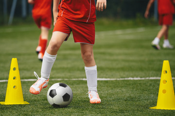 Football soccer kids team exercising with balls. Young athletes during the team training before the match. Young players in red sportswear exercises with ball and yellow cones