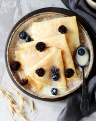 Thin pancakes with blueberries and condensed milk on a plate on a gray background