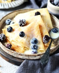 Thin pancakes with blueberries and condensed milk on a plate on a gray background