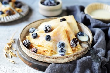 Thin pancakes with blueberries and condensed milk on a plate on a gray background
