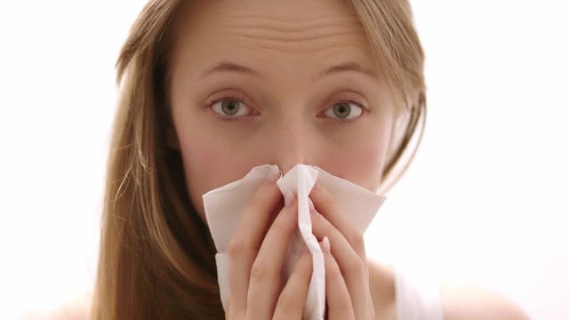Portrait of young beautiful woman having a cold. The girl blows her nose in a paper handkerchief.