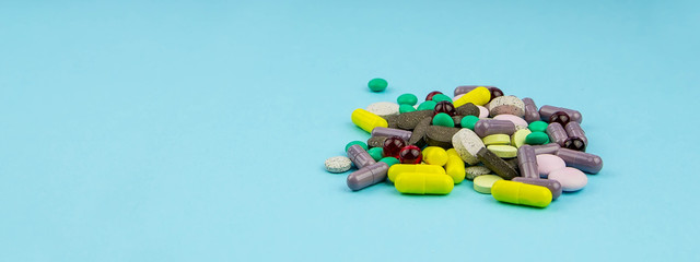 Multi-colored pills and vitamins are a bunch on a blue background. Banner with medicine.