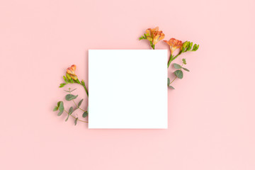 Blank paper card mockup with frame made of flowers and eucalyptus. Festive floral composition with copy space on a pink pastel background.