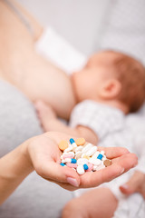 Mother holding handful of medicine while breastfeeding newborn baby