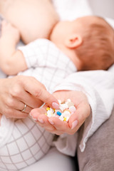 Obraz na płótnie Canvas Mother holding handful of medicine while breastfeeding newborn baby