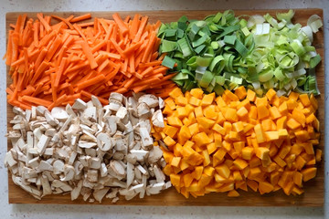 Chopped carrots, leek, red kuri squash and portobello mushroom on a wooden cutting board. Top view.