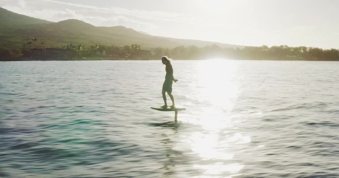 Aerial view following a man on an electric hydrofoil personal water craft surfboard riding in the ocean at sunrise, the future of electric water transportation and vehicles