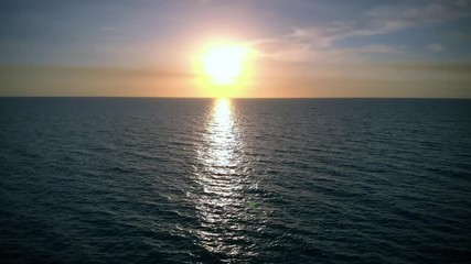Low level flight over sea at sunset, aerial view. Fly back aerial shot. Golden sun reflected on ocean surface at sunset. Aerial view of drone slide over sea surface in sun light, golden hour sunset.