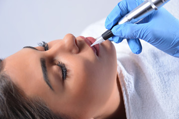 The procedure of professional applying permanent makeup on woman lips. Young beautiful girl getting...