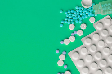 Assorted pharmaceutical medicine pills, tablets and capsules on green background