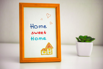Home sweet home picture in wooden frame and small houseplant on the table.