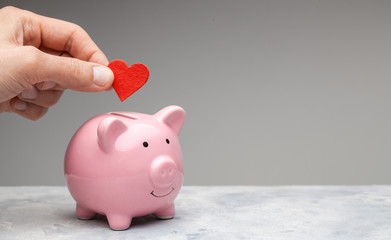 Donor. A man holds a red heart in his hand and goes to the piggy bank as a donation. Gray background