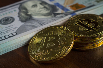 Gold coins in the form of bitcoin near a pile of hundred-dollar banknotes of a new sample