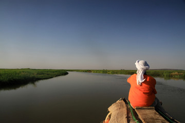 mężczyzna siedzący tyłem na końcu czółna patrzący w dal płynący spokojną rzeką niger w...