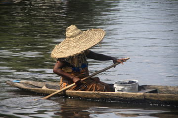 starsza czarna kobieta w dużym słomianym kapeluszu płynąca czółnem po rzece niger w mali - obrazy, fototapety, plakaty