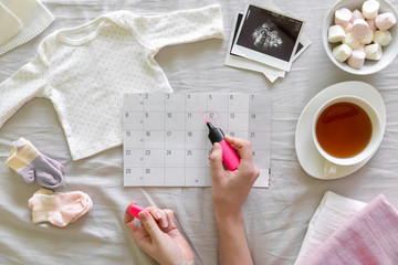 Top vew of expecting pregnant woman notes date of birth on the calendar, pregnancy and birth concept