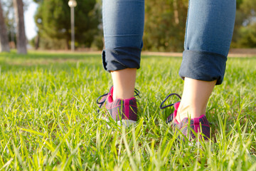 woman in running shoes walking on green and long grass