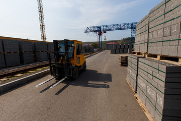 Industrial photography. A yellow forklift rides through a warehouse past pyramid-packed packages of natural stone © alexhitrov
