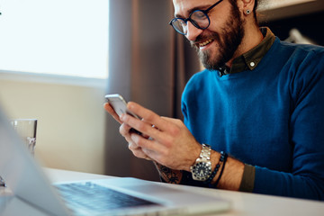 Attractive caucasian bearded entrepreneur sitting in his office, using smart phone and taking a...