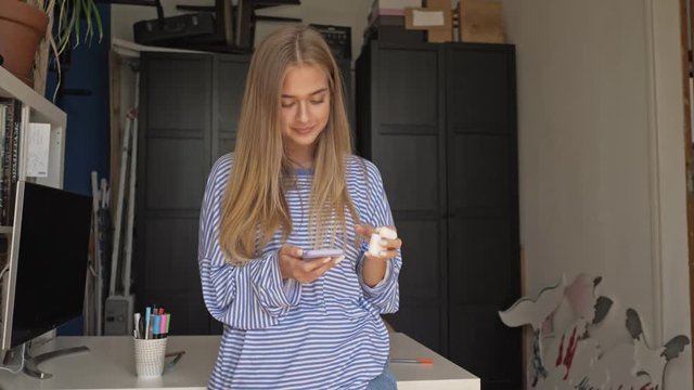 A pretty young blonde young woman is putting on her earpods in the living room