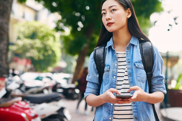 Beautiful young woman with cell phone and backpack in the city