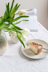 White table setting with a piece of cake and white tulips in vase