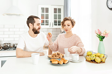 Portrait of a pretty young couple holding  croissant  while standing at the kitchen