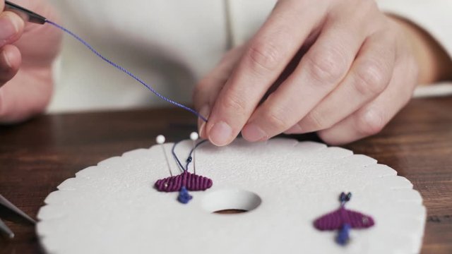 Lifestyle concept, work from home to reinvent your life: close-up of woman hands making macrame woman threads a bead into the wire with tweezers on kumihimo tools on wooden table