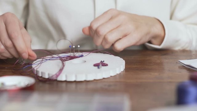Lifestyle concept, work from home to reinvent your life: close-up of woman hands making macrame knots the fuchsia thread creating an earring on kumihimo tools on wooden table