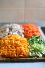 Chopped carrots, leek, red kuri squash and portobello mushroom on a wooden cutting board. Selective focus.