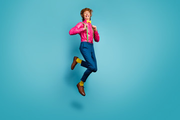 Fototapeta na wymiar Full length photo of enthusiastic cheerful guy jump enjoy spring free time holiday jump pull suspenders wear trendy pink shoes isolated over blue color background
