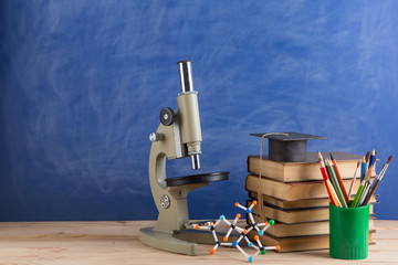 Education and sciences concept - books on the teacher desk in the auditorium, chalkboard on the background.
