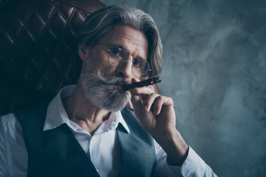 Close up photo of harsh masculine old man dandy mafiosi haughty world criminal sit leather armchair fume smoke cigarette wear grey white shirt vest isolated over concrete wall background