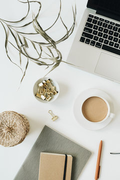Home office desk workspace with laptop, coffee cup, notebook, glasses, pen, green plant branch on white background. Flat lay, top view girl boss work business concept for lifestyle blog, social media.