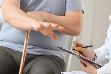 Female doctor working with senior man suffering from Parkinson syndrome in clinic