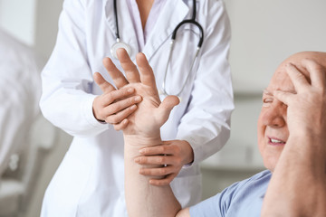 Female doctor working with senior man suffering from Parkinson syndrome in clinic