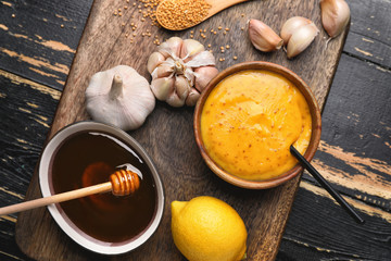 Bowl of tasty honey mustard sauce with ingredients on dark wooden background