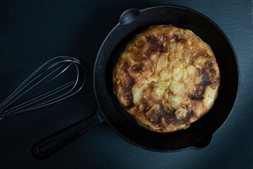 Potato and egg omelet in a frying pan and a whisk