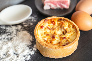 Quiche Lorraine, with spilled flour, bacon, eggs and spoon on a slate.