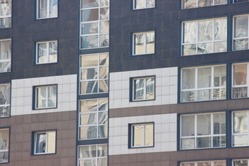 Parts of the modern facade of apartment buildings made of glass and concrete with highlights on the windows in beige colors. Trends in buildings