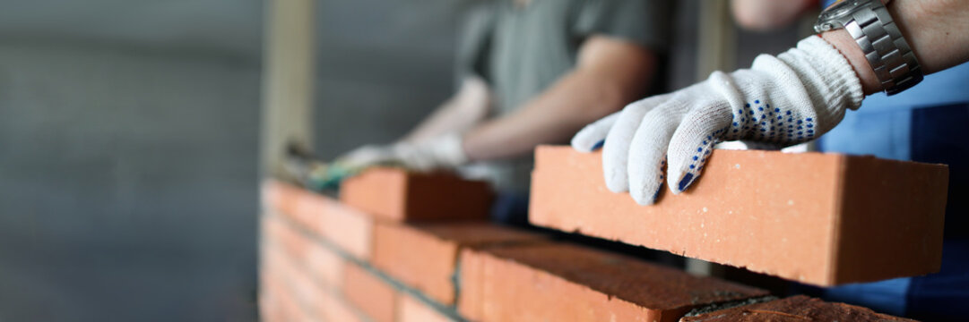 Two workers making red brick wall at construction site