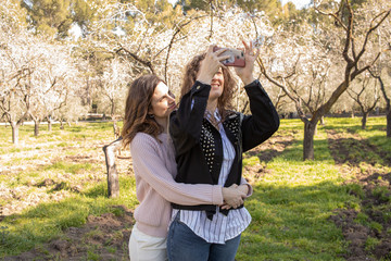 Dos chicas haciéndose selfies en un parque lleno de almendros en flor en un dia primaveral