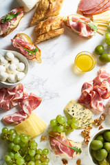 Cheese plate with brie, parmesan, cheddar and meat. Flatlay with gourmet snacks, fruits and baguette on marble board. Frame with copy space