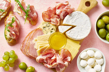 Fototapeta na wymiar A plate of appetizers for a party: cheese plate, sliced meat, crostini with pear, honey and olives. Flatlay with wine snacks on pink background